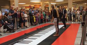 Vrouw voegt zich bij man op de vloerpiano en de menigte kijkt verbaasd toe Vrouw voegt zich bij man op de vloerpiano en de menigte kijkt verbaasd toe